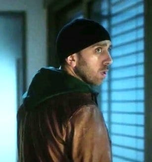 Adam wears a black beanie and brown leather jacket, whilst looking away