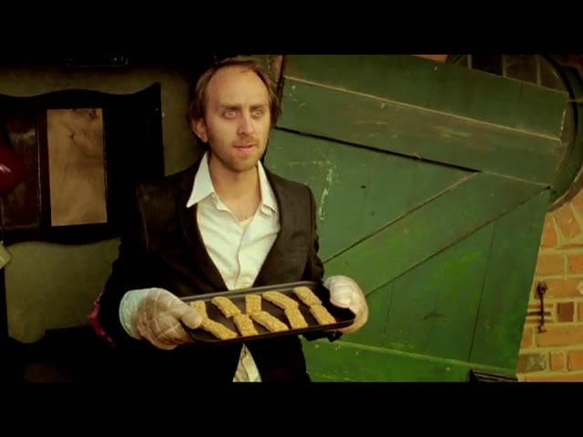 Adam wears a white shirt and dark jacket, carrying a tray of fish fingers
