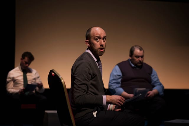 Adam is sat, looking to his right, in the National Theatre's My Country