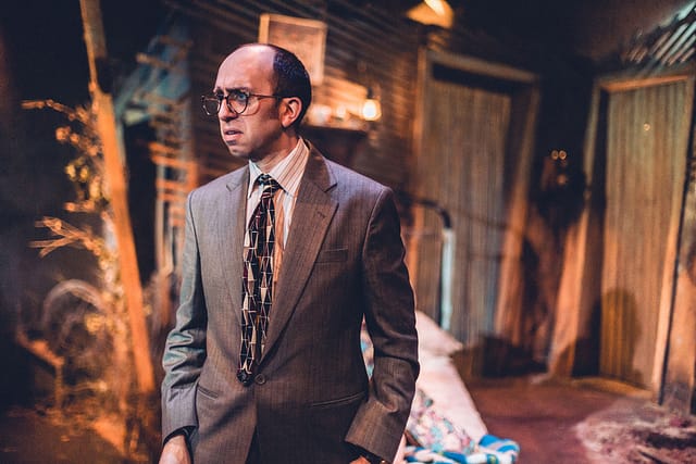 Adam wears a suit and tie while looking dismayed in African Gothic