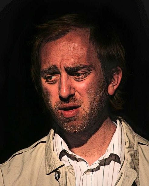 Adam wears a cream jacket, looking down and disappointed